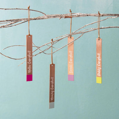 Hanging copper decorations with names on a branch against a light blue background