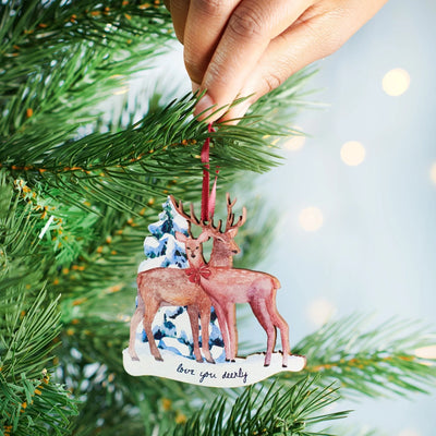 Decorative Christmas ornament with two deer and a tree, hanging from a green tree branch.