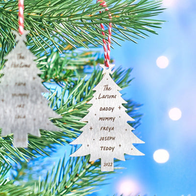 Wooden Christmas tree ornament with engraved names hanging on a tree branch with a blurred light background